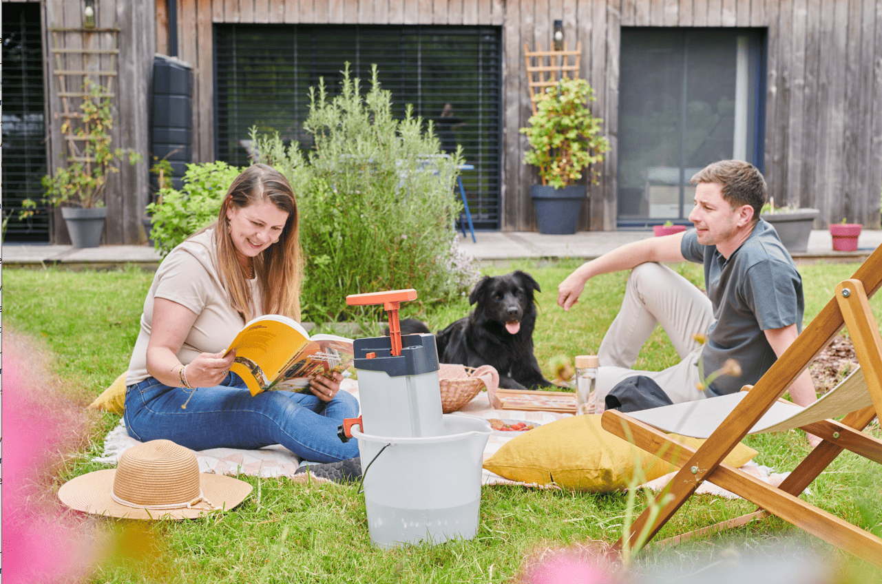 Photo d'un couple dans leur jardin avec une maison autonome, le purificateur est dans un seau et leur permet de boire de l'eau purifiée