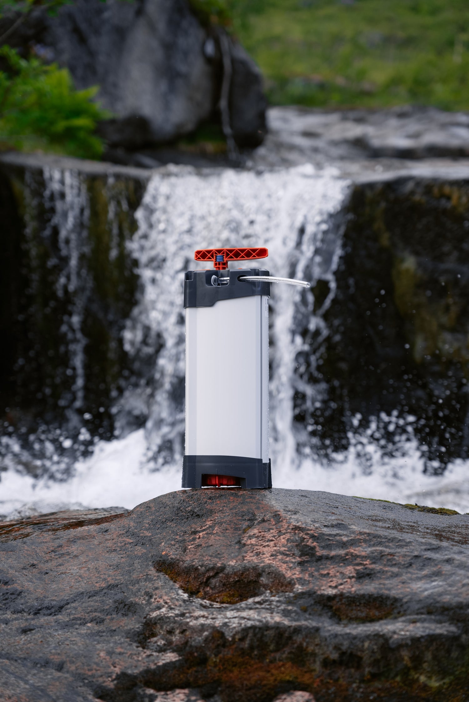 Purificateur d’eau ORISA posé sur un rocher, devant une cascade en pleine nature