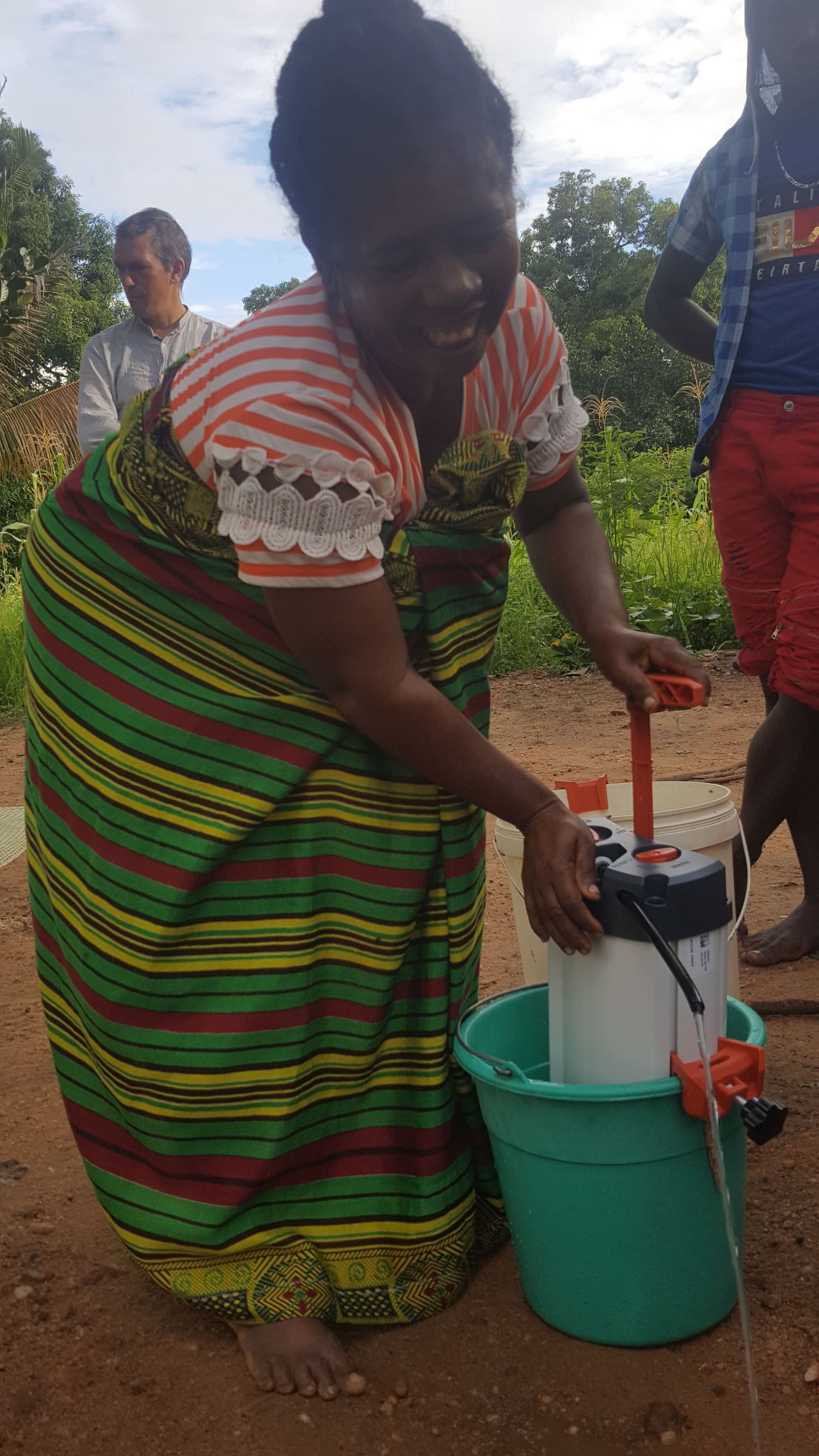 emme souriante utilisant un purificateur d’eau ORISA avec un seau, lors d’une démonstration en contexte rural à madagascar