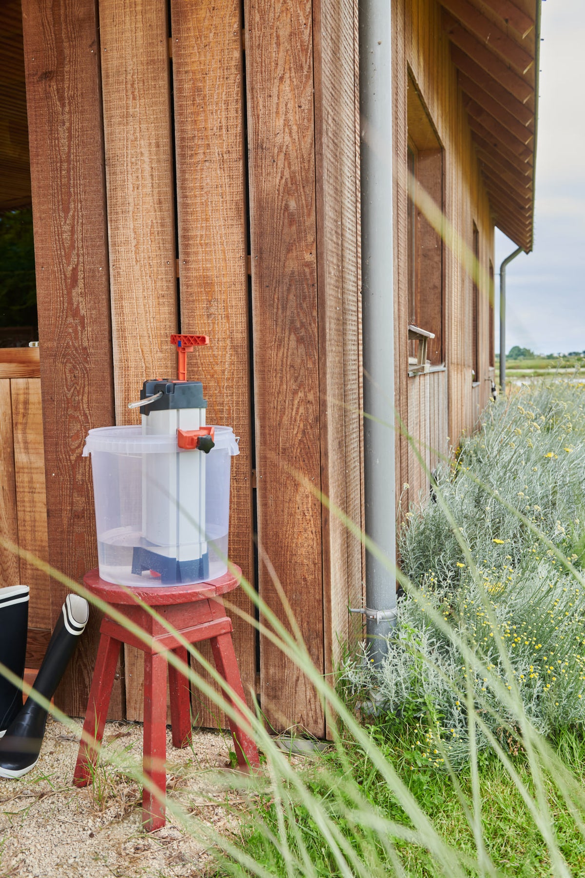 Purificateur d’eau ORISA posé dans un seau transparent sur un tabouret rouge, à l’extérieur d’un bâtiment en bois